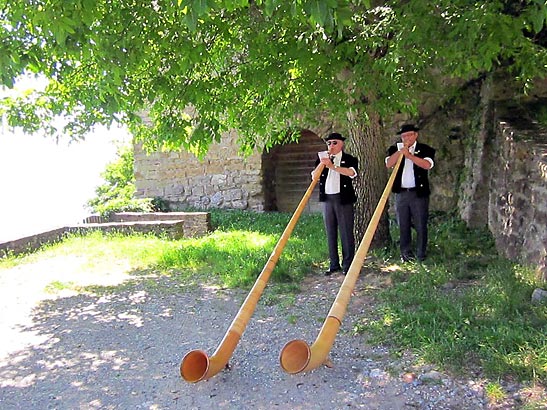 two men dressed in traditional Swiss costume playing the Alphorn