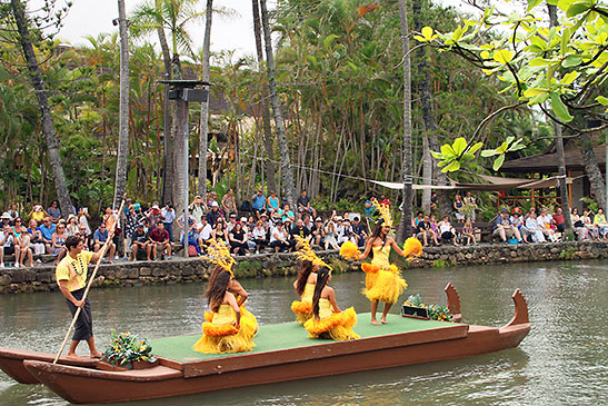 Polynesian dancers on double-hulled canoe floating down the Polynesian Cultural Center's lagoon