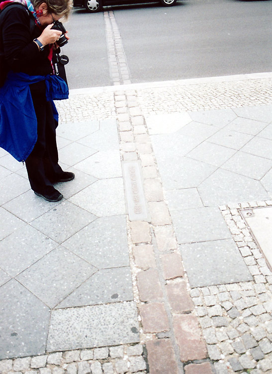 tourist taking photo of line of bricks, location of former Berlin Wall