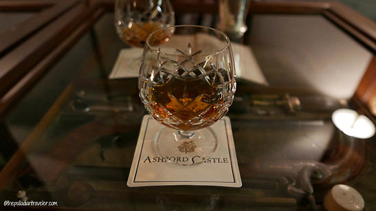 a glass of cognac on a glass table displaying antique flintlock pistols