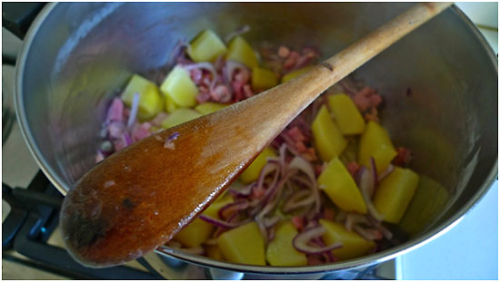 bacon cubes, chopped red onion and cubed potatoes cooking in a pot