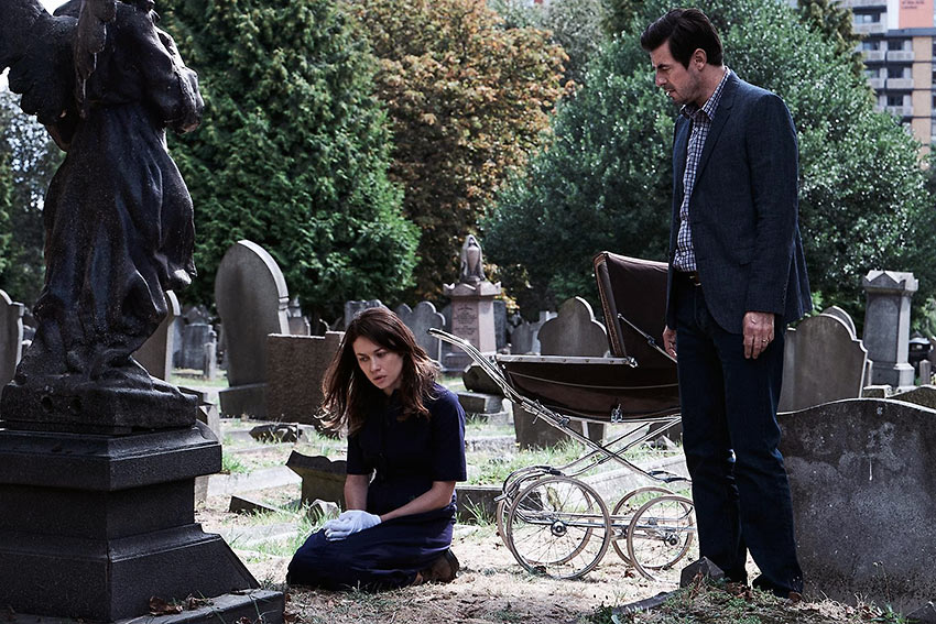 With a baby carriage looming in the background, Rosalind (Olga Kurylenko) with her husband Will (Claes Bang) visit a mystery grave